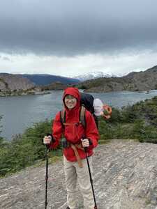 Asian man in red jacket in front of lake and mountains