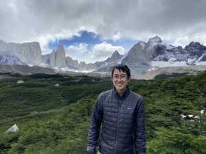 Asian man in gray jacket in front of forest and mountains