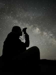 Silhouette of person using binoculars in front of stars