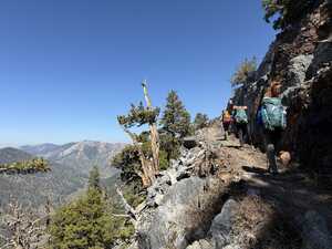 Three hikers on trail by cliff above valley