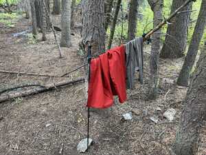 Two poles in the woods with red jacket and gray pants hanging from them