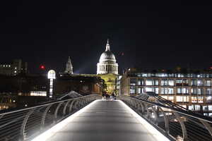 Lighted pedestrian bridge at night leading to cathedral over river