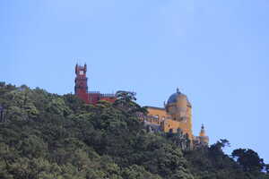 Red and yellow castle on hilltop behind trees
