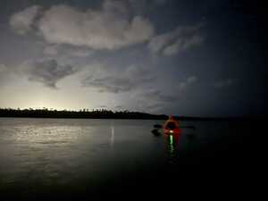 Kayak on calm waters with treeline in background at night, with clouds and stars overhead