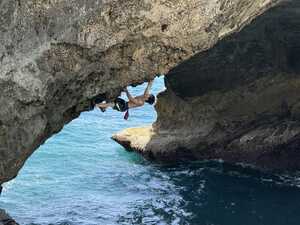 Man climbing rock upside-down above water