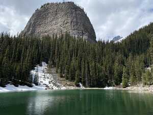 Green lake in front of pine trees and rock prominence