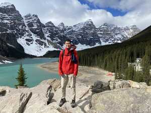 Asian man in red jacket in front of lake and mountains