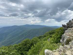 Mountaintop view overlooking forested hills with rocky outcrop to the right