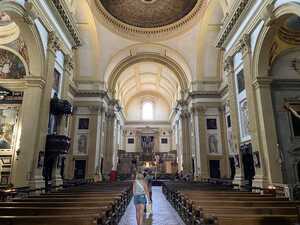 Interior of baroque church with white walls and tan square columns with pews and artwork inside