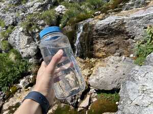 Hand holding a clear plastic bottle full of water in front of a stream