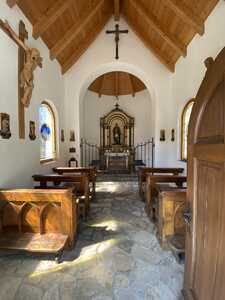 Small chapel interior with wooden pews, stone floor, and white walls