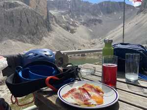 Plate of food and drinks on a picnic table with climbing gear in the mountains