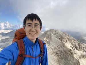 Asian man smiling in blue on mountain summit