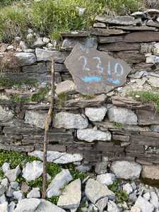 Stick propped up against stone wall with plaque with chalk writing