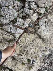 Hand holding rusted steel cable in front of rock