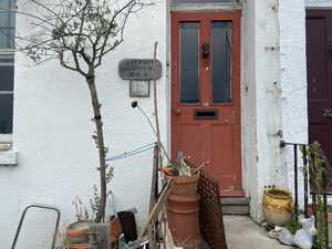 Red door on white house with scrap items in front