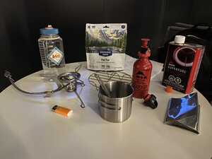 Camping stove, food, and cookware laid out on a table