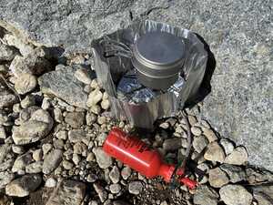 Outdoor stove with red fuel bottle on rocks