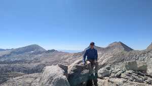 Asian man in blue sitting on a rock with mountains behind